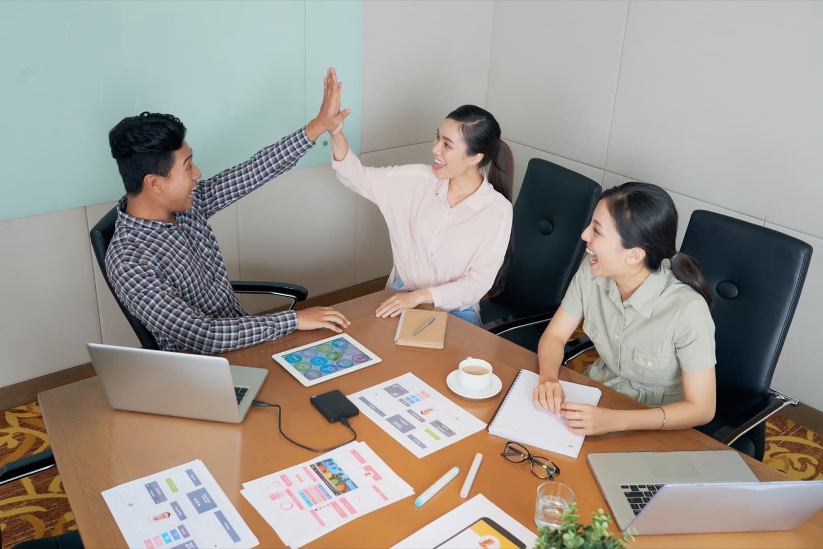Three colleagues at a meeting table high-fiving over a successful onboarding plan