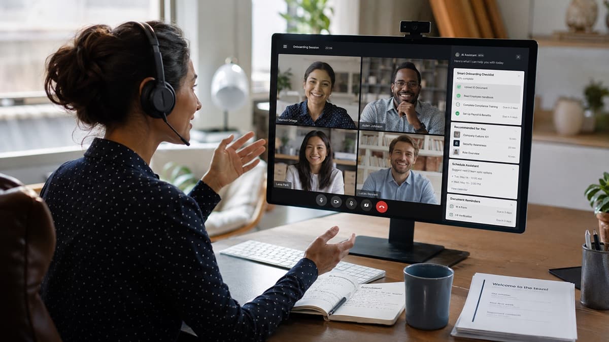 Remote worker with a headset on a video call with four smiling teammates during an onboarding session
